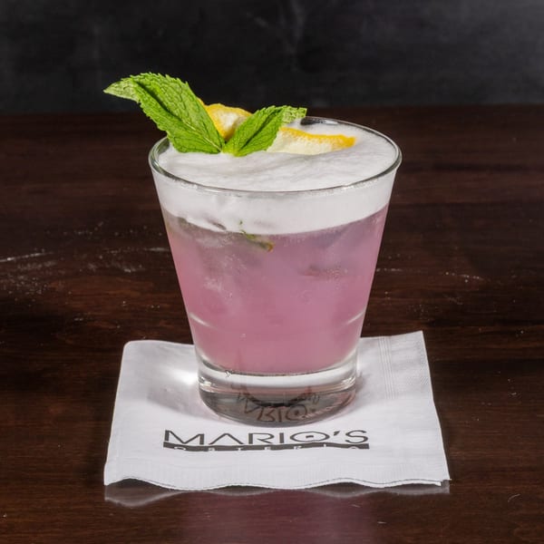 Pink cocktail with white foam, garnished with mint and lemon, on a Mario's Osteria napkin.