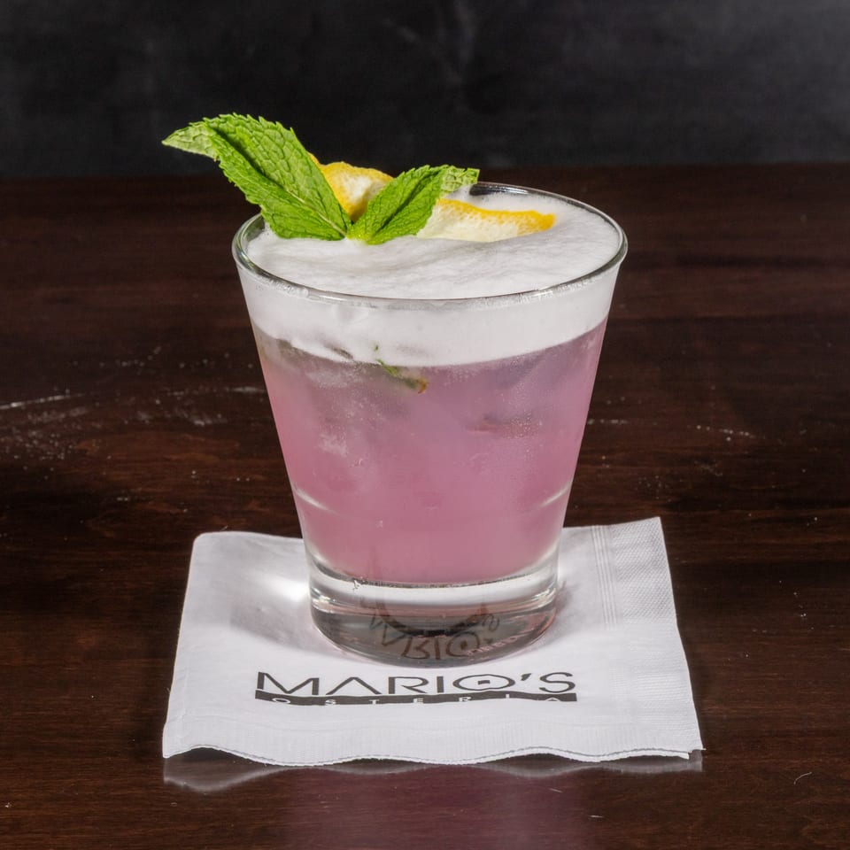 Pink cocktail with white foam, garnished with mint and lemon, on a Mario's Osteria napkin.
