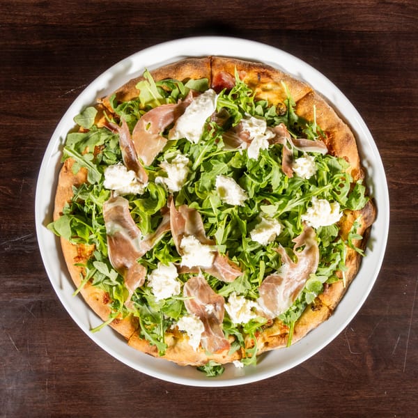 Overhead view of a pizza topped with fresh arugula, prosciutto, and dollops of ricotta cheese.