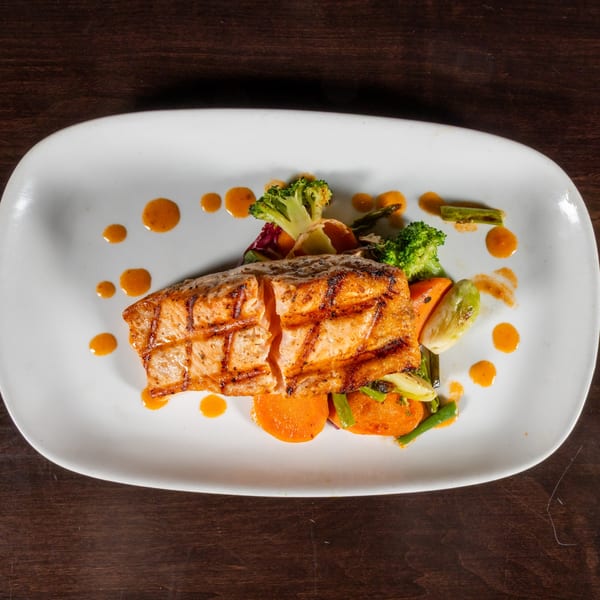 Grilled salmon with broccoli, carrots, and asparagus, drizzled with orange sauce on a white plate.