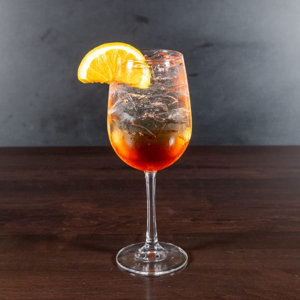 A vibrant orange cocktail with ice and an orange slice garnish, on a dark wooden table.