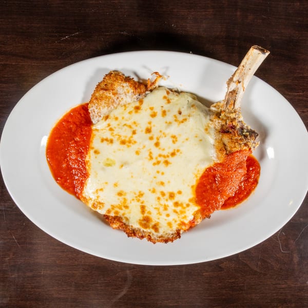 Breaded pork chop with bone, covered in melted cheese and marinara sauce on a white plate.