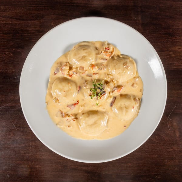 Lobster ravioli in a creamy sauce with diced lobster and microgreens on a white plate.