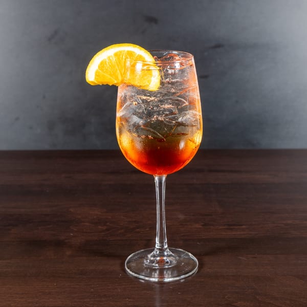 A vibrant orange cocktail with ice and an orange slice garnish, on a dark wooden table.