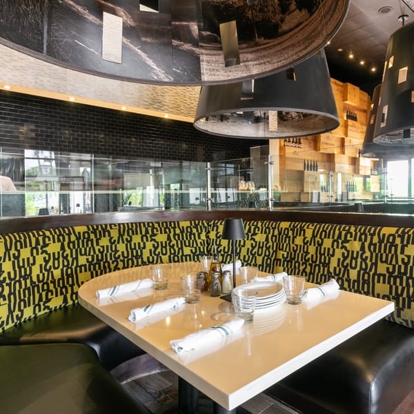 Restaurant interior with a set table, yellow and black patterned booth, and modern light fixtures.