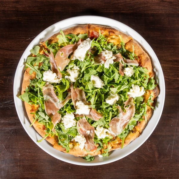 Overhead view of a pizza topped with fresh arugula, prosciutto, and dollops of ricotta cheese.