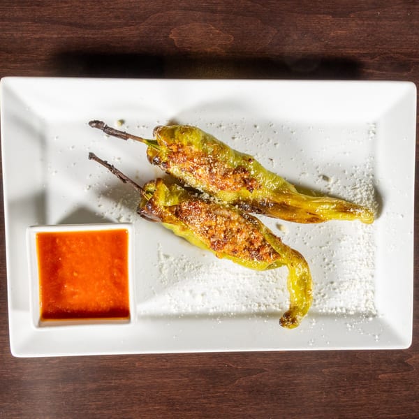 Two stuffed green peppers with cheese and a side of red sauce on a white plate.
