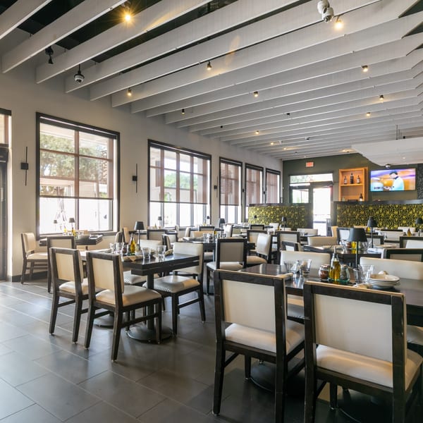 Spacious restaurant dining room with dark tables, light chairs, large windows, and a patterned wall.