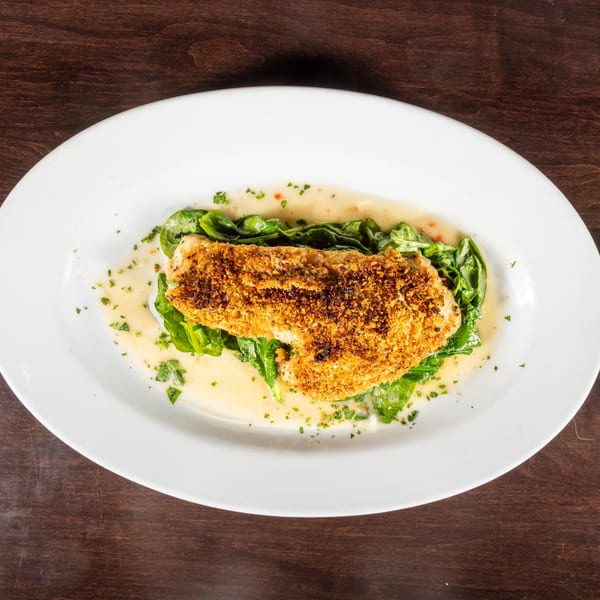 Crispy breaded fish fillet on a bed of spinach with a creamy sauce, garnished with herbs.
