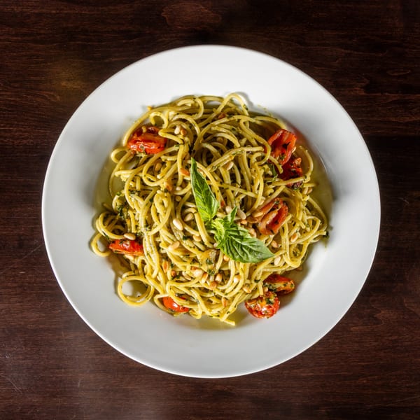 Spaghetti with pesto, cherry tomatoes, pine nuts, and fresh basil on a white plate.