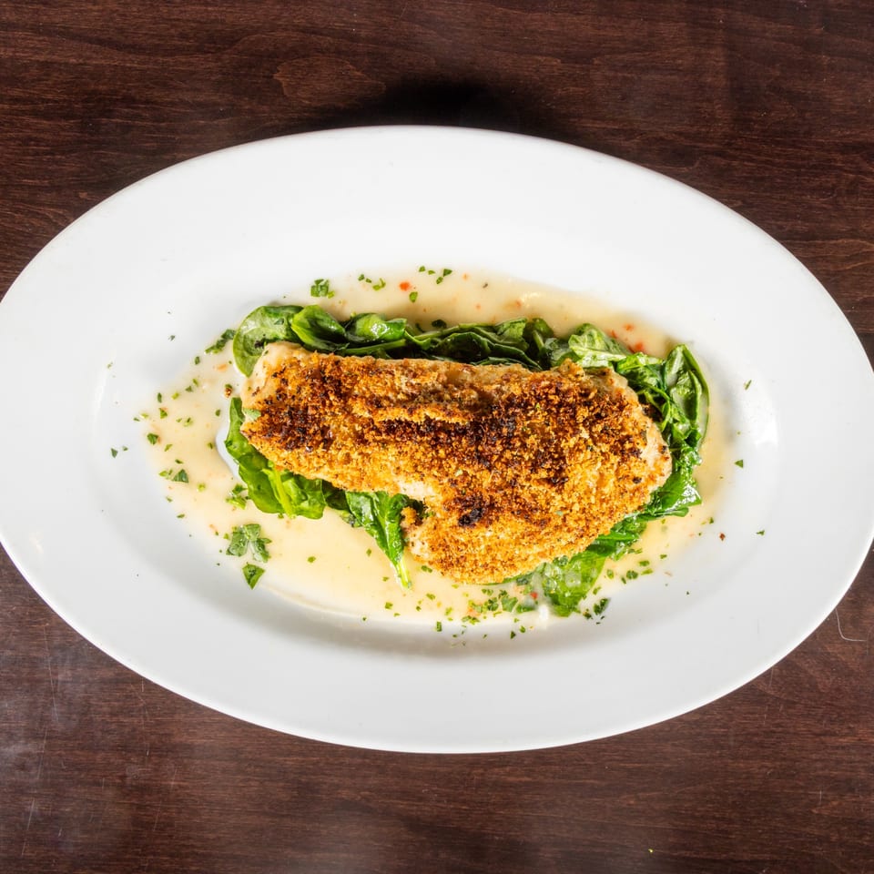 Crispy breaded fish fillet on a bed of spinach with a creamy sauce, garnished with herbs.
