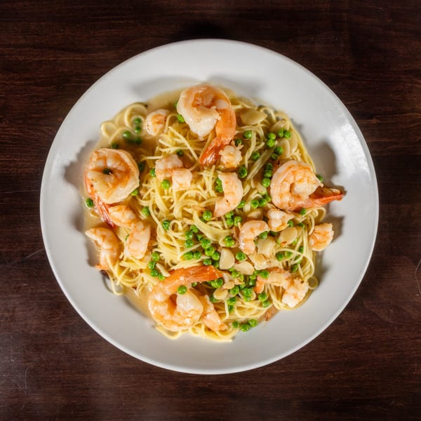 Shrimp scampi with linguine, peas, and sliced garlic in a white wine sauce on a white plate.