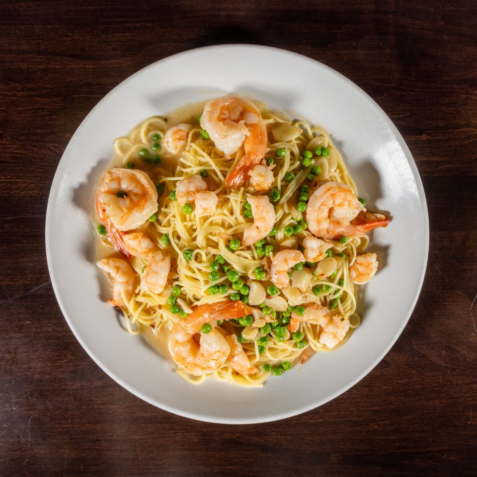 Shrimp scampi with linguine, peas, and sliced garlic in a white wine sauce on a white plate.