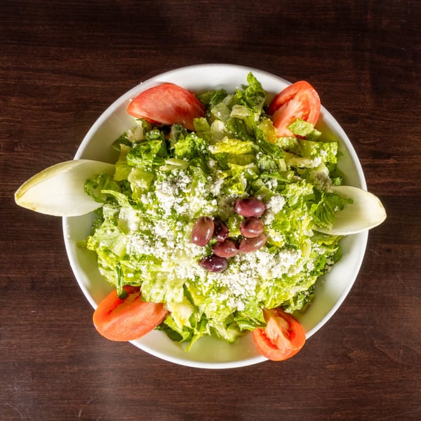 Overhead view of a fresh green salad with tomatoes, olives, and crumbled cheese in a white bowl.