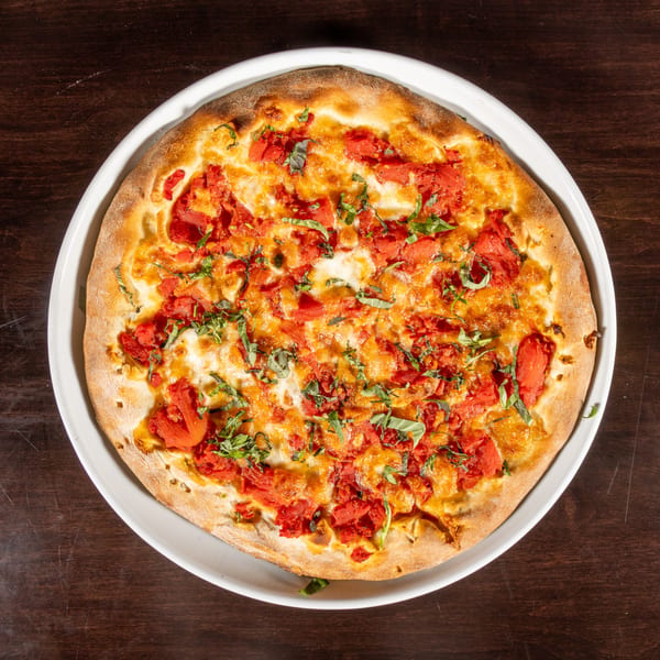 A whole round pizza with red tomatoes, melted cheese, and fresh basil on a white plate.