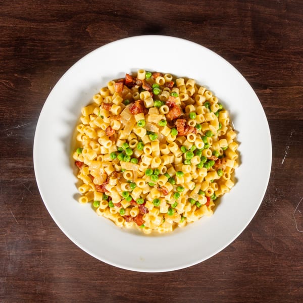 Ditalini pasta with peas, onions, and bacon in a light sauce on a white plate.