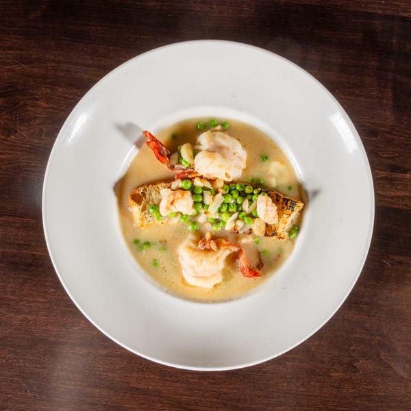 Overhead view of a white bowl with shrimp, peas, and garlic in a creamy sauce with toasted bread.
