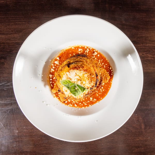 Eggplant parmesan with red sauce, cheese, and basil on a white plate.