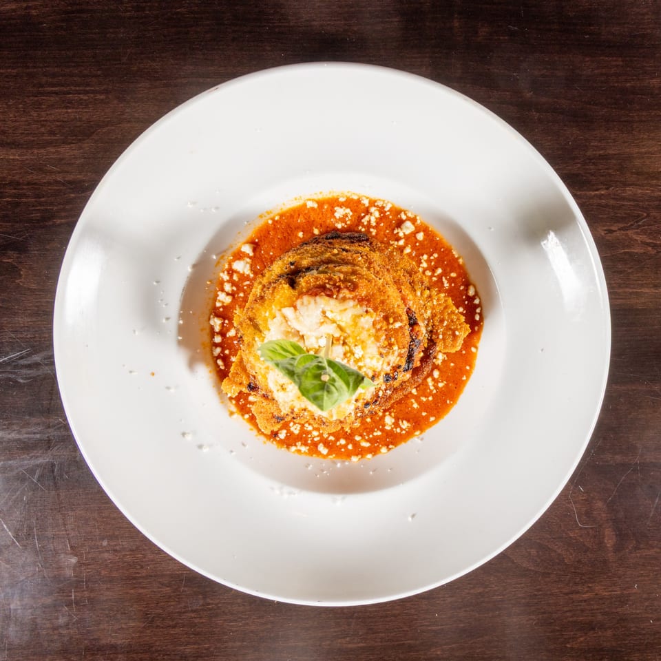 Eggplant parmesan with red sauce, cheese, and basil on a white plate.