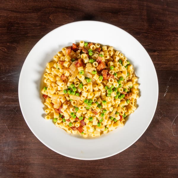 Ditalini pasta with peas, bacon, and onions in a creamy sauce on a white plate.