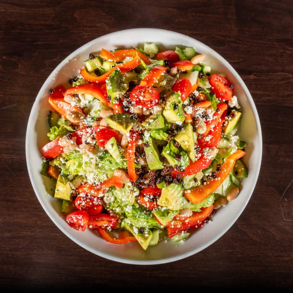 A vibrant salad with lettuce, red peppers, avocado, tomatoes, beans, and crumbled cheese.
