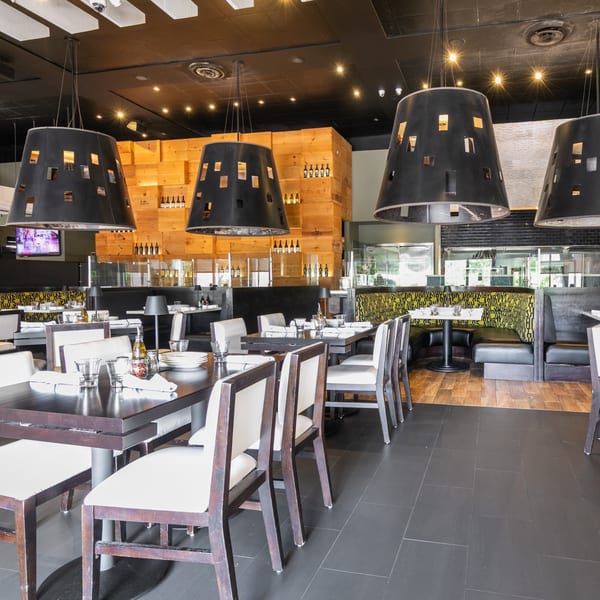 Modern restaurant interior with dark tables, white chairs, black booths, and large black pendant lights.
