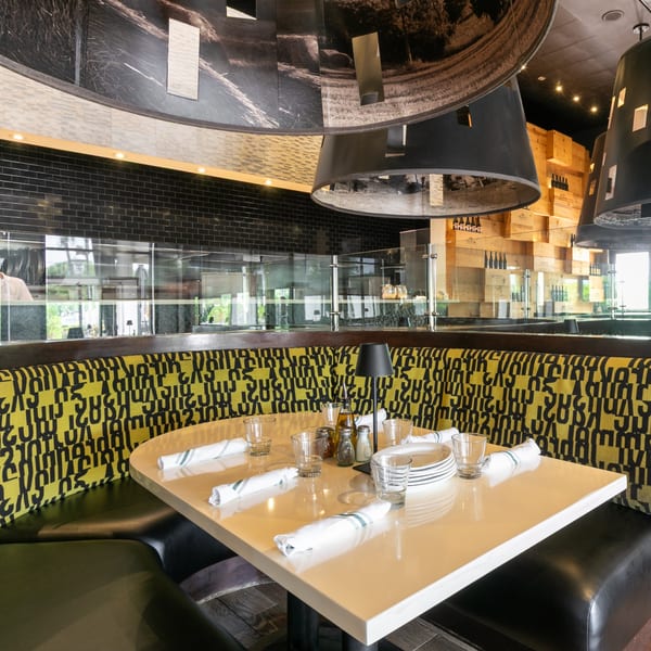 A restaurant booth with a yellow and black patterned backrest, set with plates, glasses, and napkins.