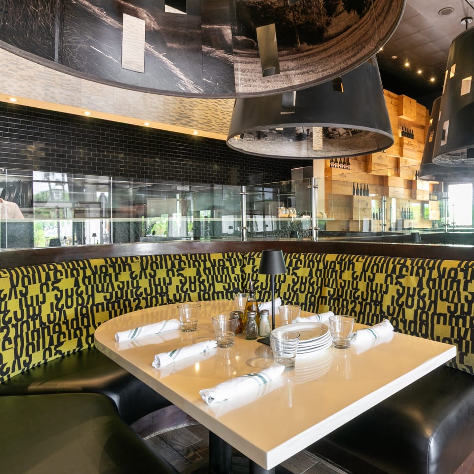 A restaurant booth with a yellow and black patterned backrest, set with plates, glasses, and napkins.