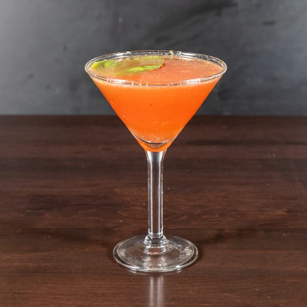 A vibrant orange cocktail with a green garnish in a martini glass on a dark wooden table.