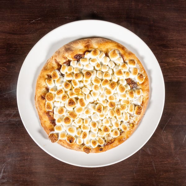 Overhead view of a dessert pizza with toasted marshmallows and a golden crust on a white plate.